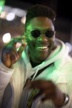 Greenlit African man wearing sunglasses at night as shade of anonymity, approved immigration,