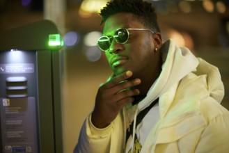 Thoughtful greenlit African man at parking ticket machine pausing as symbol for approved