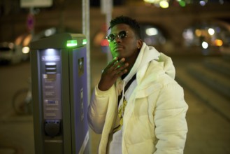 Thoughtful greenlit African man at parking ticket machine pausing as symbol for approved