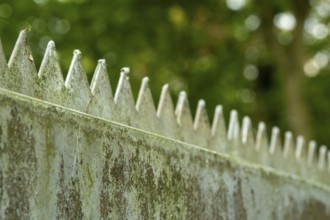Borken, NRW, Germany, Metal security fence with sharp spikes against green bokeh creating a