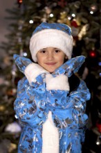 Smiling little girl wearing a blue snegurochka costume in front of a christmas tree.Belarus