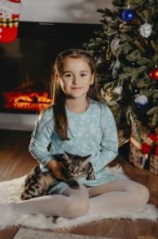 Young girl holding a kitten by a fireplace during festive winter holiday.Belarus