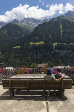 A couple sitting on a bench is enjoying the view on the mountains in Champery, a village in