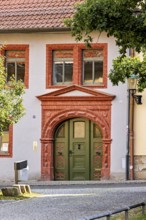 Historic building façade with green door and decorative red stone decorations, surrounded by trees