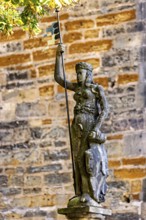 Statue of a figure carrying a flag and a shield in front of an old stone wall, statue and monument