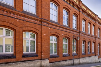 Classic red brick façade of a building with white windows under a blue sky, brick façade of
