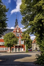 Historic building with tower and red accents, surrounded by trees, The old town of Arnstadt in