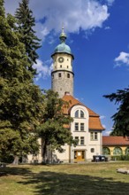 Tower with clock and building in the foreground, surrounded by trees under a blue sky, The Niedeck