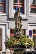 Stone figure on a fountain with surrounding flowers in front of a building, statue and monument in