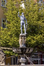 Metal statue of a warrior on a fountain surrounded by green trees, statue and monument in the old