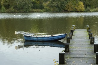Borken-Hoxfeld, NRW, Germany, A blue boat rests calmly at the edge of a wooden dock on a quiet lake