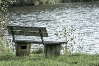 Wooden bench sitting by grassy lake shore offering quiet solitude and relaxation, Borken, nrw,