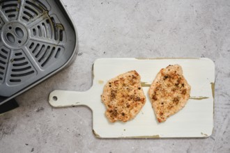 Juicy pork loin cutlets sit on a cutting board after being cooked in an air fryer. These tender