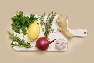 Fresh parsley, lemon, red onion, garlic, ginger, thyme, and rosemary on a chopping board ready for