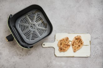 Two perfectly cooked pork sirloin chops rest on a cutting board beside an air fryer basket. The