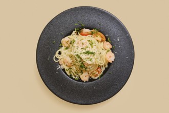 Delicious creamy garlic shrimp pasta in a black plate, garnished with herbs and cheese. This