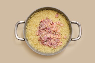 A pot with cooked risoni pasta and fresh shrimps. The dish features a creamy texture and vibrant