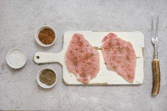 Two pork sirloin chops on a cutting board, seasoned with various spices, in a well-lit kitchen.