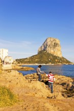 Two people on a rocky coast, natural park, in the background rock Penon de Ifach, landmark,