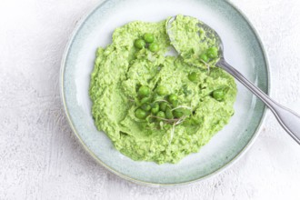 A vibrant green pea puree fills a shallow bowl, topped with fresh peas and microgreens. The dish