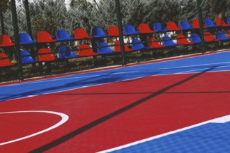 A brightly colored basketball court features bold red and blue sections under the clear sky.