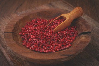 Bright red peppercorns, in a wooden bowl, with a small wooden tray