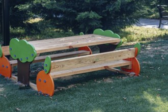 A vibrant wooden picnic table with colorful tree designs stands in a green park, surrounded by
