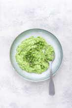 A vibrant green pea puree fills a shallow bowl, topped with fresh peas and microgreens. The dish