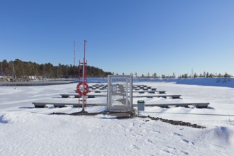 Empty marina with snow covered docks and ground with frozen sea ice on a cold winter day in sunny