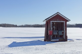 Old weathered red hut with three mail boxes by rural road in winter with snow covering the ground,