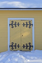 Old wooden double doors with wrought iron decorative hinges in winter with snow on the ground,