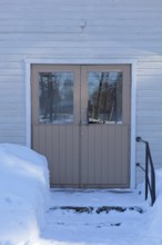 Double doors and steps on a old wood building in winter with snow on the ground, Vastila, Finland