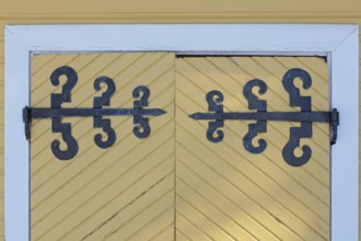 Closeup of old wrought iron decorative hinges on yellow painted wooden doors, Suurikylä, Finland