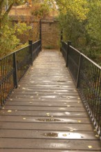 Wooden plank bridge extending through a park with autumn foliage, wet from recent rain, with