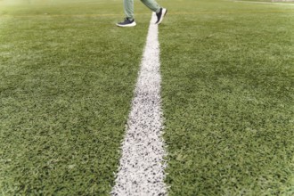 Person walking across a white line on a green artificial turf soccer field, representing progress