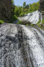 Two waterfalls flowing over rocks surrounded by green vegetation in sunny nature, Jermuk Waterfall,