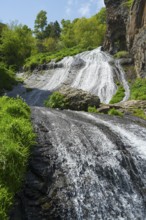 A multi-tiered waterfall and green plants create an idyllic natural landscape in the sun, Jermuk