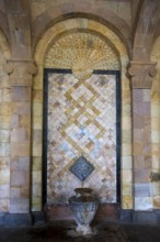 Detailed mosaic with decorative patterns and reliefs on the wall above a stone jug, spring, mineral