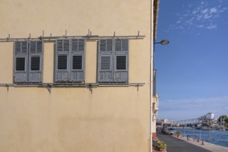 Yellow house façade with three gray wooden shutters to move and a view across the Canal de Sete