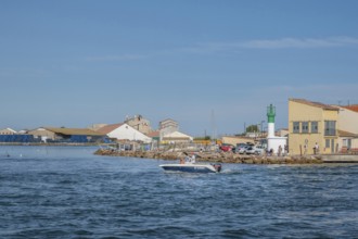 A motorboat with people on board steering it sails in front of the white-green little lighthouse