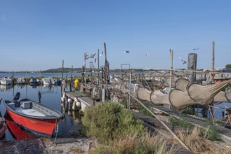 A red fishing boat is lying in the foreground on a wooden pier where numerous fish traps and nets