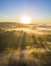 Sunrise over a fog covered village in a rural landscape, golden morning light, serene autumn