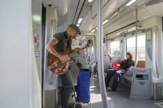 Musician busker playing guitar onboard train of Rodalia de Barcelona suburban rail network,