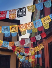 A vibrant display of colorful papel picado decorations hanging across a narrow Mexican street,