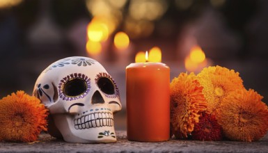 A beautifully decorated Día de Muertos sugar skull is placed beside a burning candle and vibrant