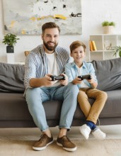 A man and a boy are sitting on a couch playing video games. The man is smiling and the boy is