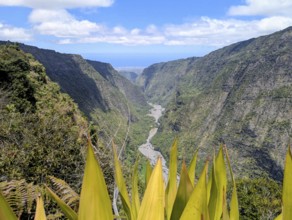 Scenic valley with a river, flanked by steep mountains and lush greenery beneath a partly cloudy