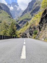 Paved road leading through a mountainous landscape beneath a cloudy sky, La Réunion, France