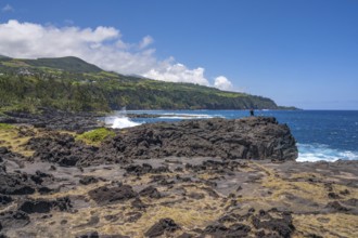 An angler stands on a massive rock of the black lava coast and looks out at the roaring Indian