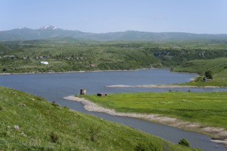 Winding river flows into a lake surrounded by green hills under a blue sky, Kechut Reservoir,
